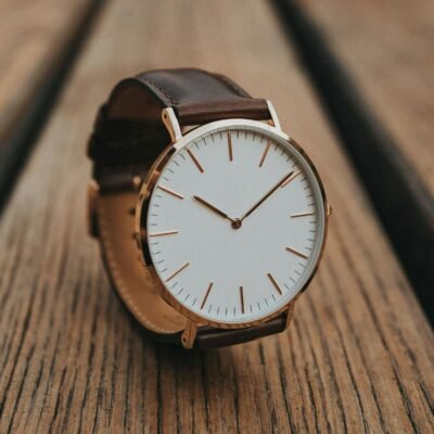 Close-up of a minimalist analog watch with brown leather strap on a wooden surface.