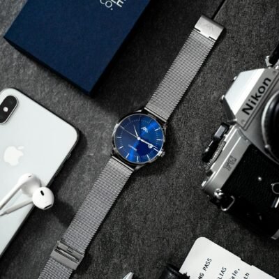 Stylish flat lay showcasing technology devices, watch, and accessories on dark surface.