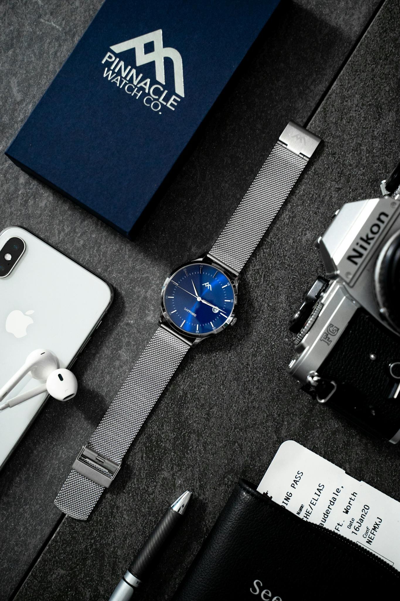 Stylish flat lay showcasing technology devices, watch, and accessories on dark surface.